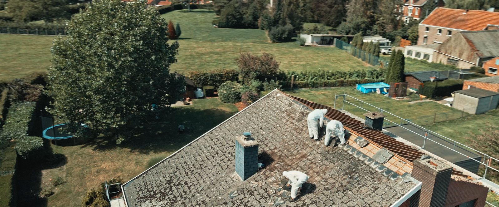 Asbestverwijderaars in beschermende kleding aan het werk op een woningdak